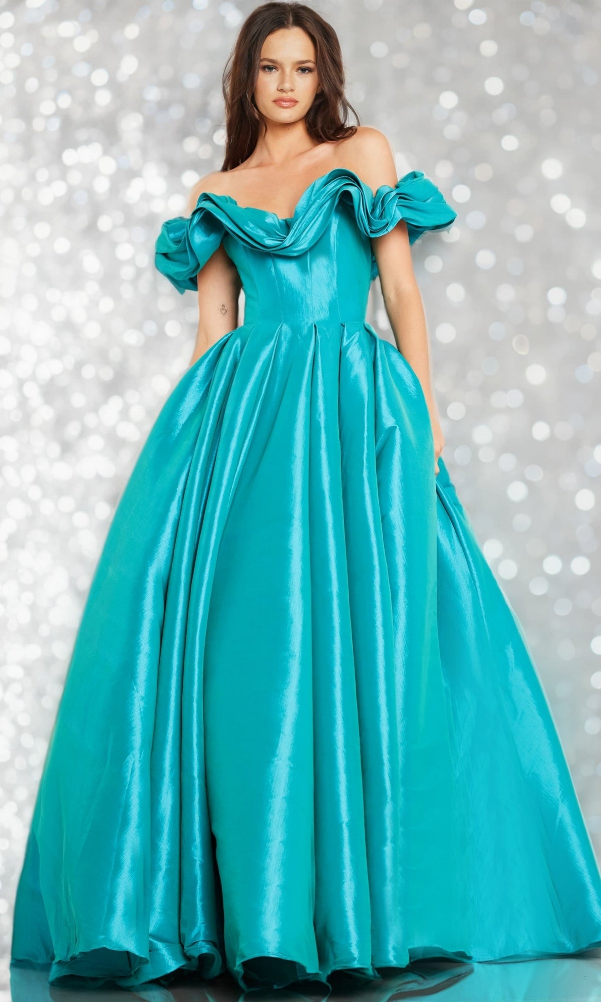 A woman poses against a sparkling, blurred light background in the Long Prom Dress 37476 by Jovani—an off-shoulder ball gown with ruffled sleeves, crafted from elegant teal taffeta in a flattering A-line silhouette.